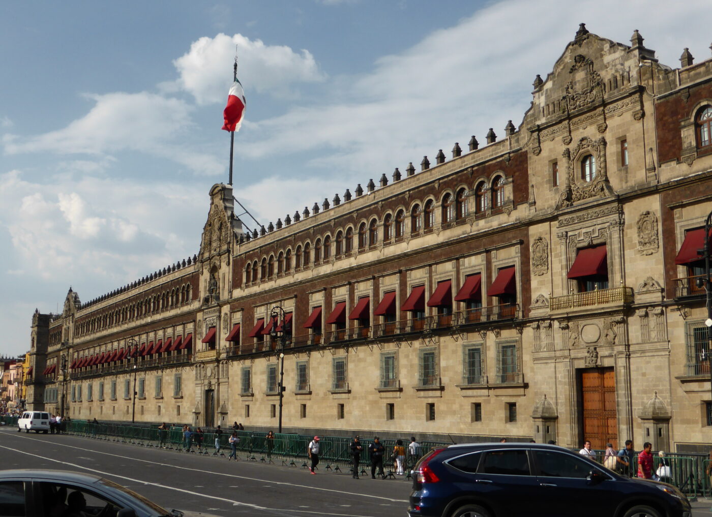 Ciudad de México: Palacio Nacional con bandera ondeando. Arquitectura colonial, Houm expande oficinas en ciudades clave. Fachada histórica y cielo parcialmente nublado.