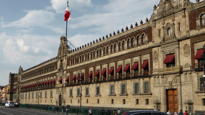 Ciudad de México: Palacio Nacional con bandera ondeando. Arquitectura colonial, Houm expande oficinas en ciudades clave. Fachada histórica y cielo parcialmente nublado.