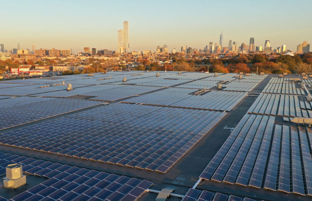 Paneles solares en techo de edificio logístico con horizonte urbano. Energía solar para real estate logístico, impacto y sostenibilidad. Vista aérea.