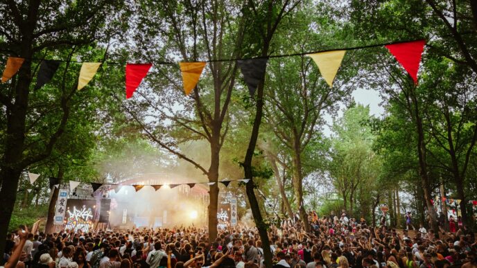 Festival musical sostenible en Londres: Multitud disfrutando de la música en vivo bajo banderines coloridos entre árboles. Impacto en el real estate.