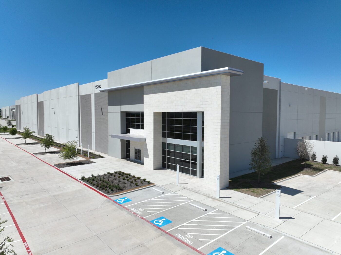 Fachada de instalaciones de supercomputación IA en Texas. Edificio gris moderno con estacionamiento accesible. Inauguración de tecnología avanzada.