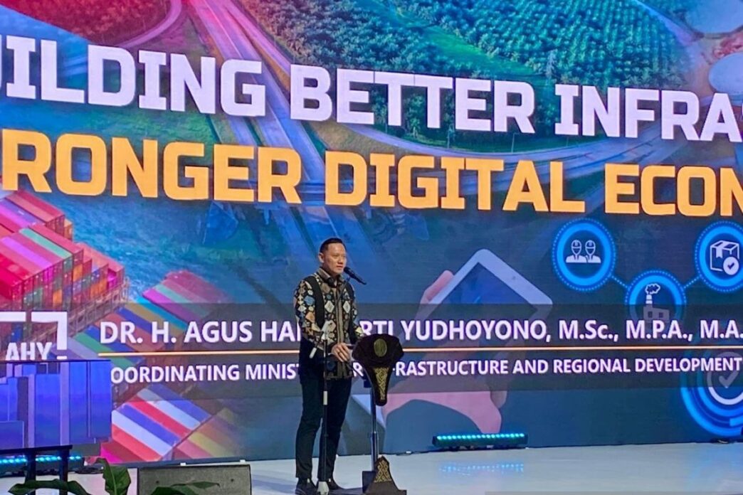Indonesia impulsa infraestructura digital y talento: Hombre en pódium frente a pantalla con texto "Building Better Infra, Stronger Digital Econ"