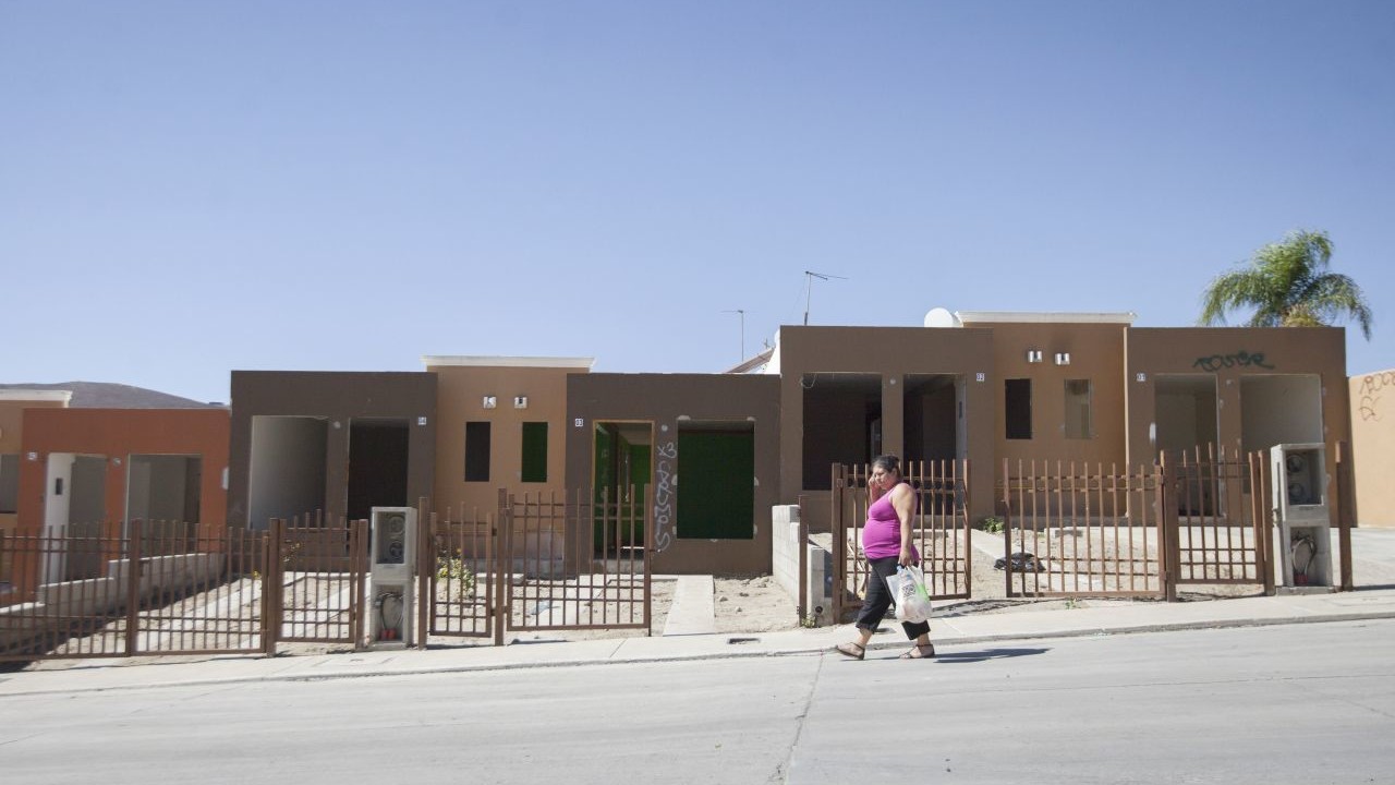 city/destination
Una mujer camina frente a casas de interés social en México. Vivienda económica, desarrollo urbano, ciudad, bienes raíces.