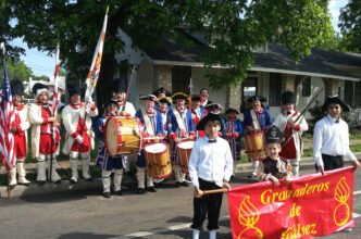 Desfile de los Granaderos de Gálvez en EE.UU. Músicos y participantes portan banderas. Evento cultural mexicano en la ciudad.