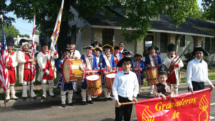 Desfile de los Granaderos de Gálvez en EE.UU. Músicos y participantes portan banderas. Evento cultural mexicano en la ciudad.
