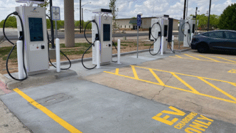 Estación de carga EV moderna con varios puntos, señalización clara y un coche eléctrico. Infraestructura clave para el Real Estate sostenible.
