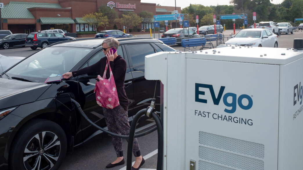 Una mujer carga su coche eléctrico en una estación de carga EVgo frente a un supermercado. Infraestructura EV transformando el sector inmobiliario.