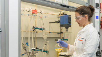 Investigadora Build-Limonene en laboratorio, experimentando con materiales de construcción sostenibles. Probeta con líquido amarillento en manos enguantadas.