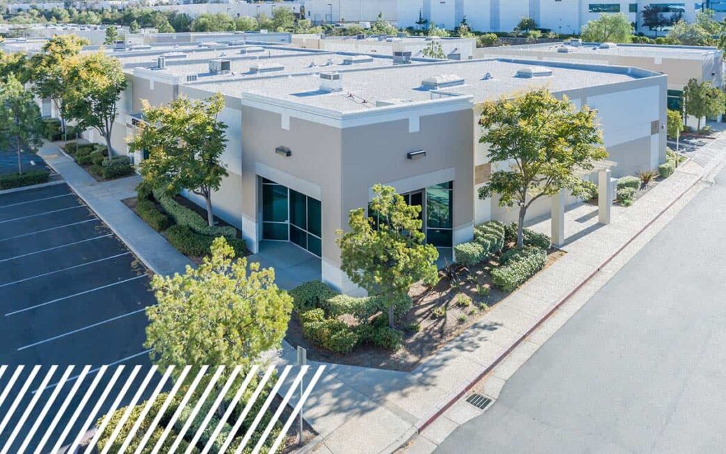 Vista aérea de edificio comercial moderno para innovación inmobiliaria con drones, estacionamiento amplio y vegetación. Transformación del sector.