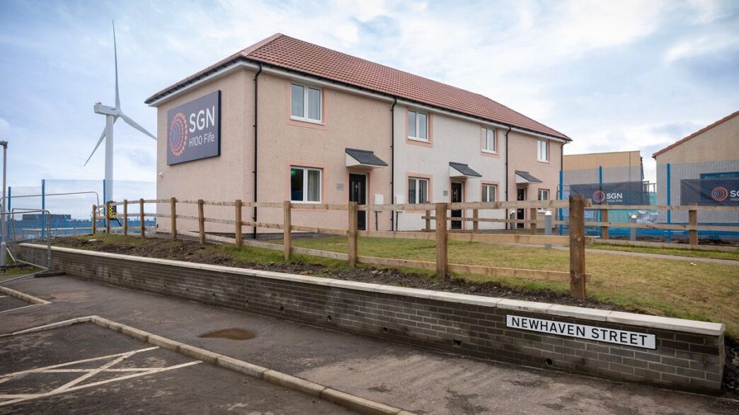 Innovación en Hidrógeno Verde: Casas en Alemania con energía sostenible. Aerogenerador y letrero SGN H100 Fife. Real Estate transformado por hidrógeno.