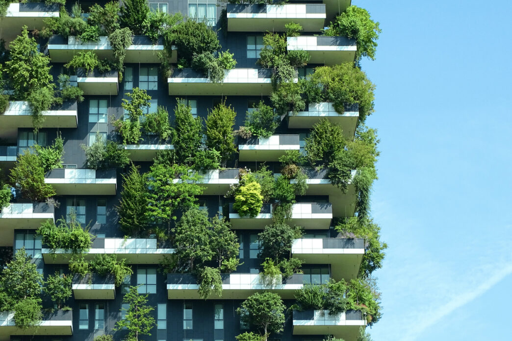 Edificio innovador con balcones llenos de vegetación, ejemplo de materiales que reducen riesgos en real estate. Fachada verde y cielo azul.