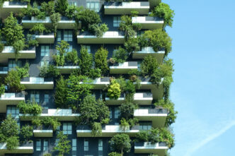 Edificio innovador con balcones llenos de vegetación, ejemplo de materiales que reducen riesgos en real estate. Fachada verde y cielo azul.