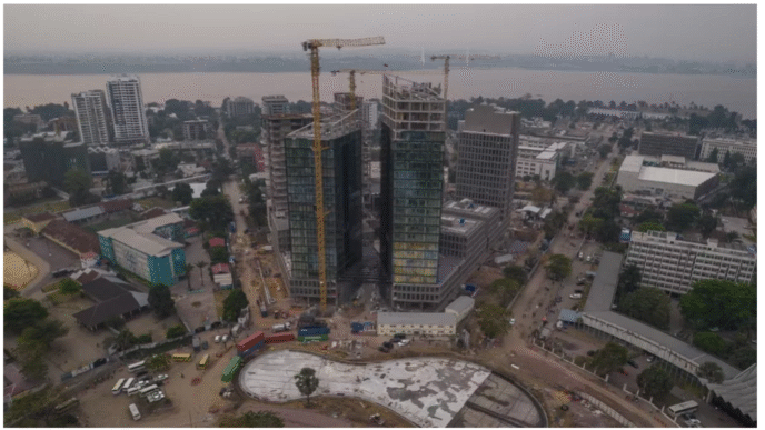 Vista aérea del centro financiero en construcción en RDC, destacando la innovación en el transporte verde y el desarrollo urbano. Grúas y edificios.