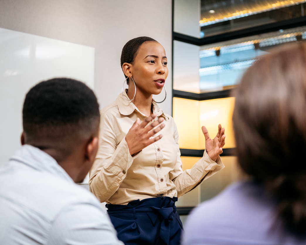 Mujer afroamericana liderando una presentación sobre innovación en Real Estate. Expresión facial y gestos indican liderazgo y transformación empresarial.