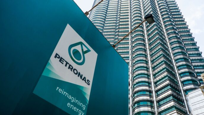 Primer plano del logo de PETRONAS frente a las torres gemelas, destacando innovaciones sostenibles en infraestructura petrolera. Re-imaginando energía.