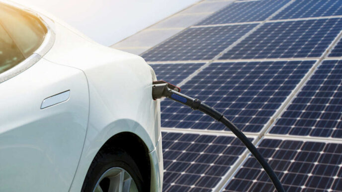 Carga EV con energía solar: coche eléctrico blanco cargando frente a paneles solares. Integración solar y carga EV para real estate sostenible.