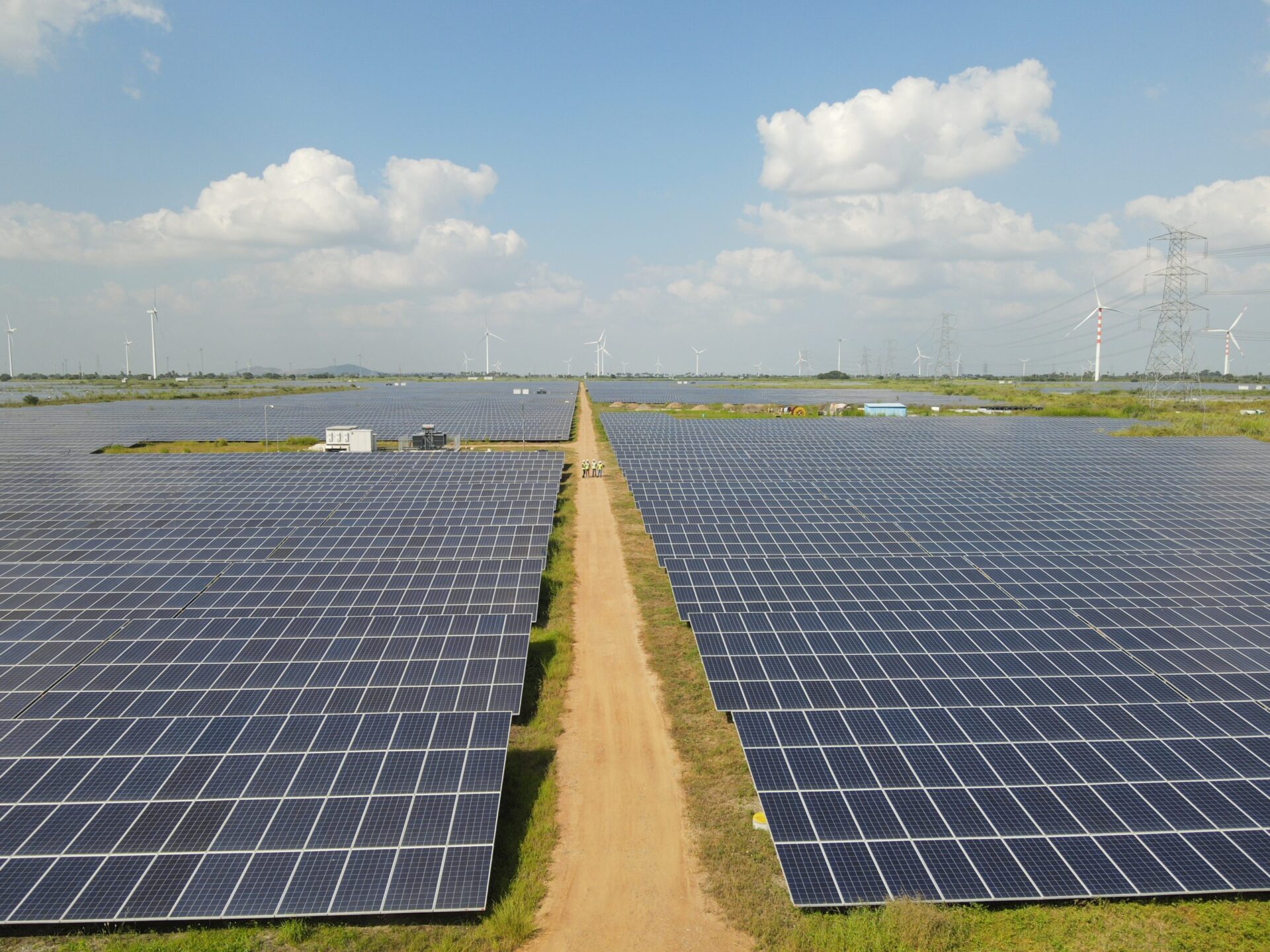 Amplia vista de parque solar con paneles azules y turbinas eólicas al fondo. Inversión en Blueleaf Energy impulsa infraestructura verde. BII.