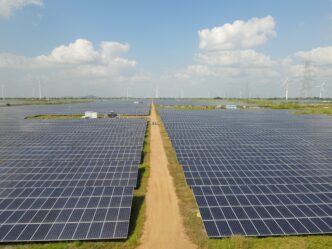 Amplia vista de parque solar con paneles azules y turbinas eólicas al fondo. Inversión en Blueleaf Energy impulsa infraestructura verde. BII.