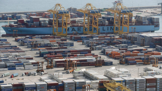 Vista aérea del puerto con buque Maersk, grúas y contenedores. Impacto en la inversión logística y retail en España. Descenso del 42%.