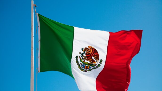 Bandera ondeante de México contra un cielo azul, simbolizando la Inversión Extranjera Directa de Turismo en México y su impacto positivo.