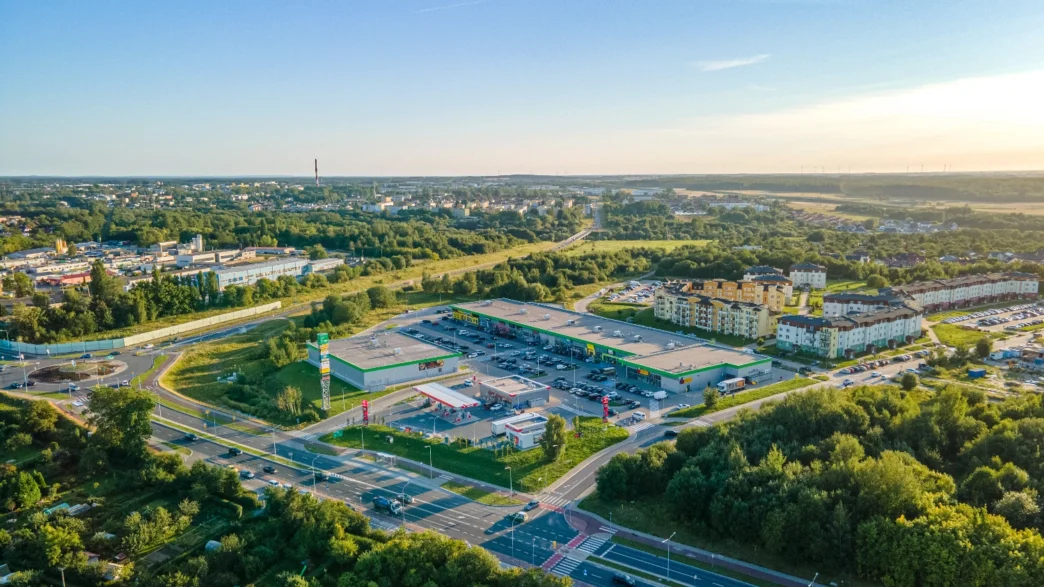 Vista aérea de inversión sostenible en real estate polaco: centro comercial con parking, gasolinera y edificios residenciales en un entorno verde.