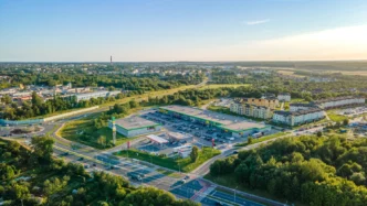 Vista aérea de inversión sostenible en real estate polaco: centro comercial con parking, gasolinera y edificios residenciales en un entorno verde.