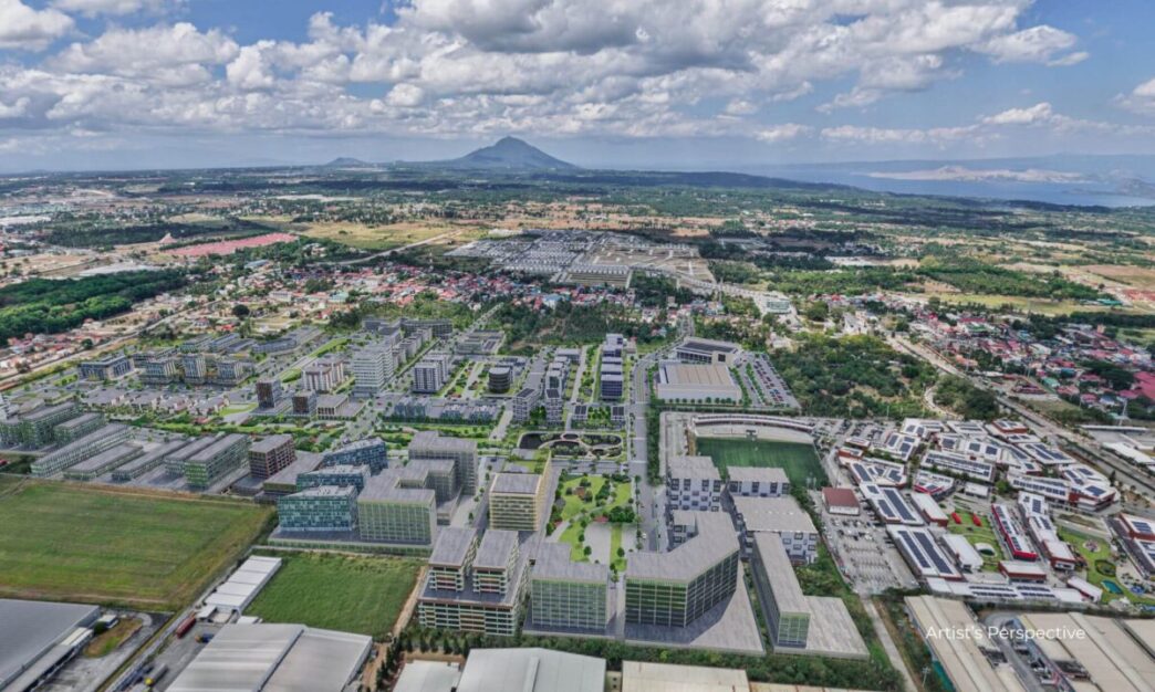 Vista aérea de Meadow at LIMA Estate, Batangas. Inversiones sostenibles, edificios modernos, paisaje urbano y monte en el horizonte.