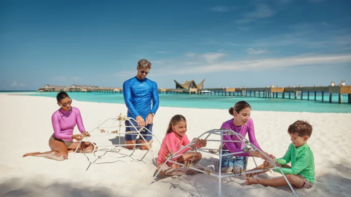 Familia construye estructura en JOALI Maldives, mostrando sostenibilidad y compromiso EarthCheck Gold. Resort paradisíaco con playa y agua turquesa.