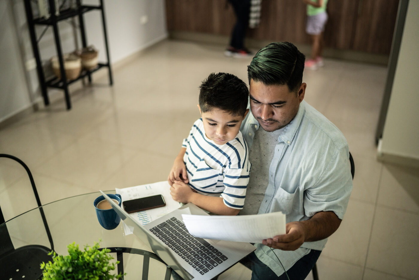 Joven mexicano con hijo revisando documentos en laptop, analizando opciones para adquirir o rentar vivienda. Retos de vivienda para jóvenes en México.