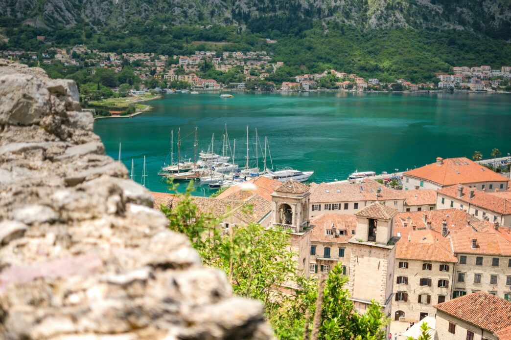Vista panorámica de Kotor, joya arquitectónica del Mediterráneo. Casas de tejas rojas, bahía azul turquesa y montañas verdes. Destino turístico ideal.