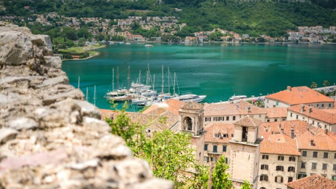 Vista panorámica de Kotor, joya arquitectónica del Mediterráneo. Casas de tejas rojas, bahía azul turquesa y montañas verdes. Destino turístico ideal.