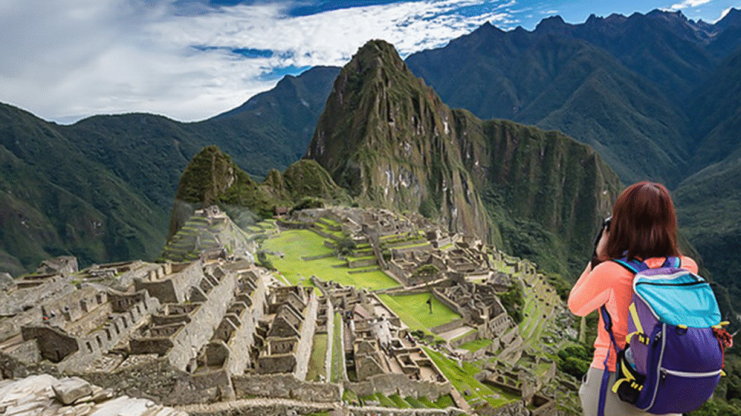 Turista capturando la majestuosidad de Machu Picchu, impulso al turismo en Nuevo León. Montañas imponentes y ruinas antiguas en un paisaje andino único.