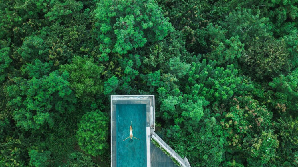 Vista aérea de piscina rodeada de vegetación exuberante, fusionando lujo y sostenibilidad en la arquitectura. Diseño moderno y armonía con la naturaleza.