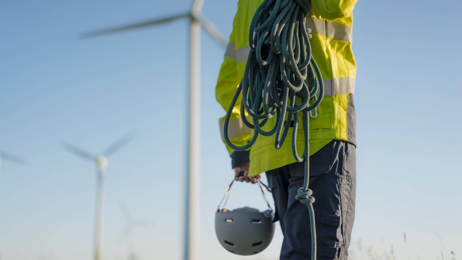 Obrero con cuerda y casco frente a turbinas eólicas. Brecha de habilidades verdes en el sector inmobiliario sostenible y energías renovables.