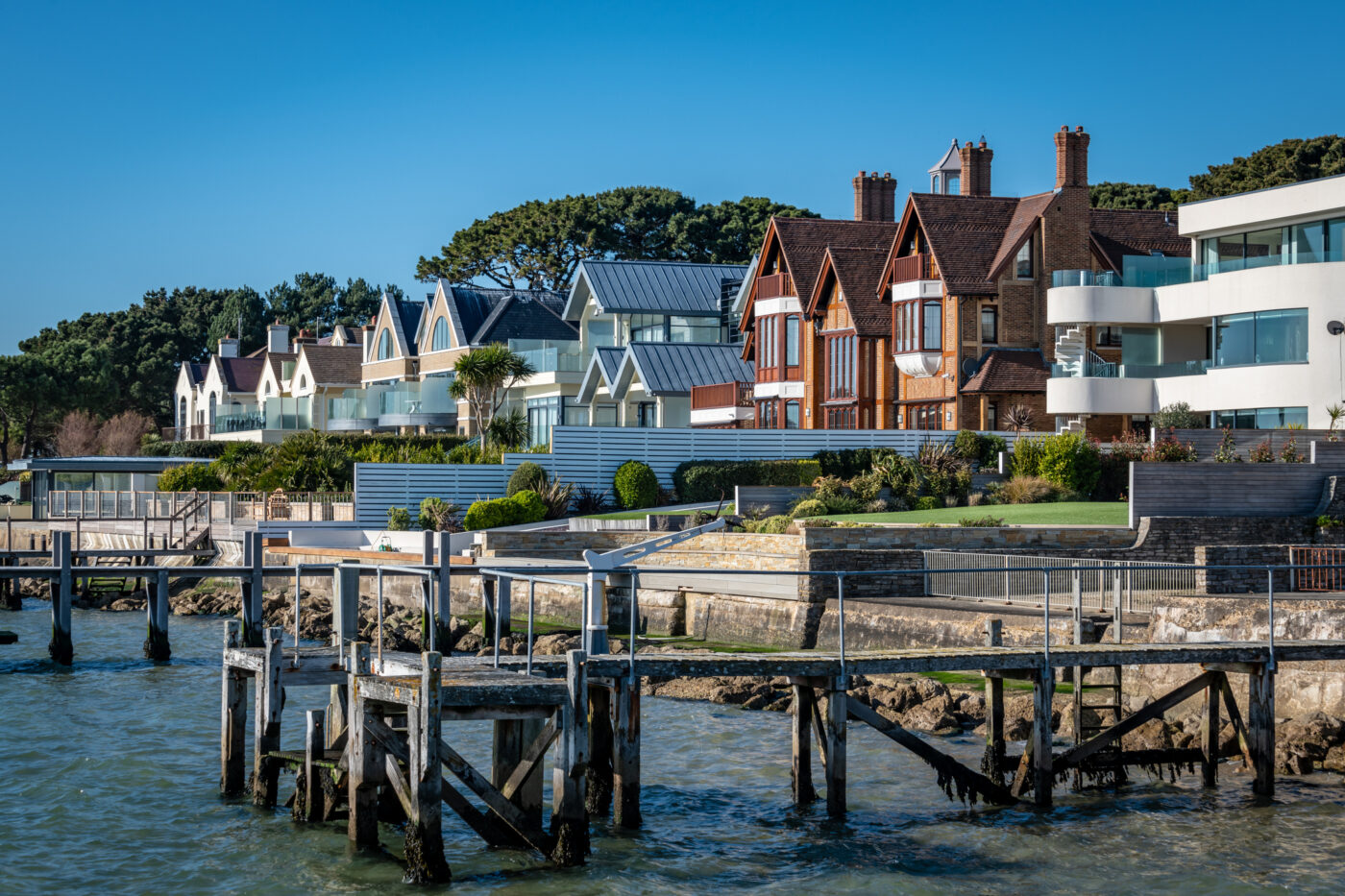 Sandbanks: Refugio en la fila de los millonarios. Vistas de casas exclusivas desde el muelle. Arquitectura de lujo en la costa, jardines cuidados.