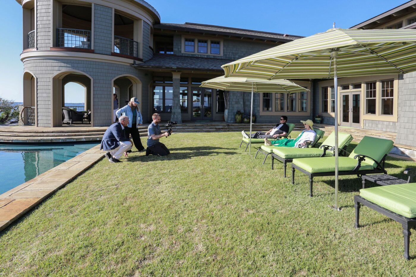 Escena de filmación de marketing inmobiliario de lujo con equipo junto a piscina y personas relajándose en tumbonas. Evolución del marketing.