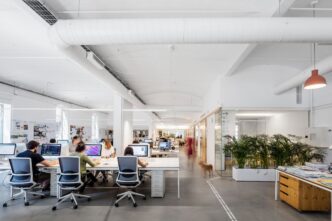 Espacio diáfano de PMMT Arquitectura con mesas de trabajo y personal. Diseño innovador y sostenible en construcción para oficinas modernas y eficientes.