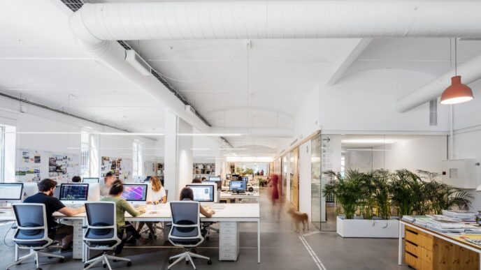 Espacio diáfano de PMMT Arquitectura con mesas de trabajo y personal. Diseño innovador y sostenible en construcción para oficinas modernas y eficientes.