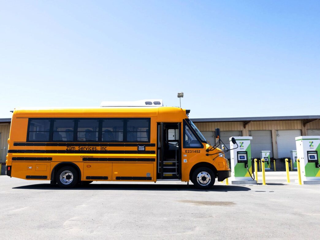 Autobús escolar eléctrico amarillo Zum Services en estación de carga. Innovación en movilidad eléctrica para el transporte escolar italiano.