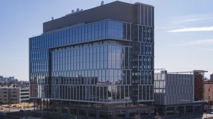 Edificio LEED Platinum en Somerville con diseño innovador y sostenible. Arquitectura moderna con fachada de vidrio reflejando el cielo azul.