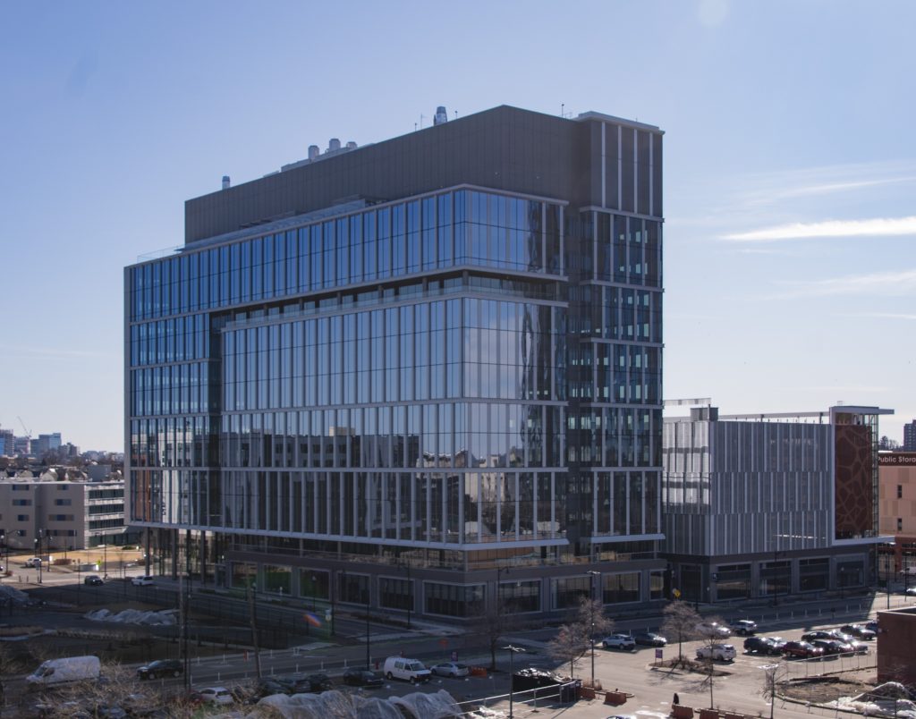 Edificio LEED Platinum en Somerville con diseño innovador y sostenible. Arquitectura moderna con fachada de vidrio reflejando el cielo azul.