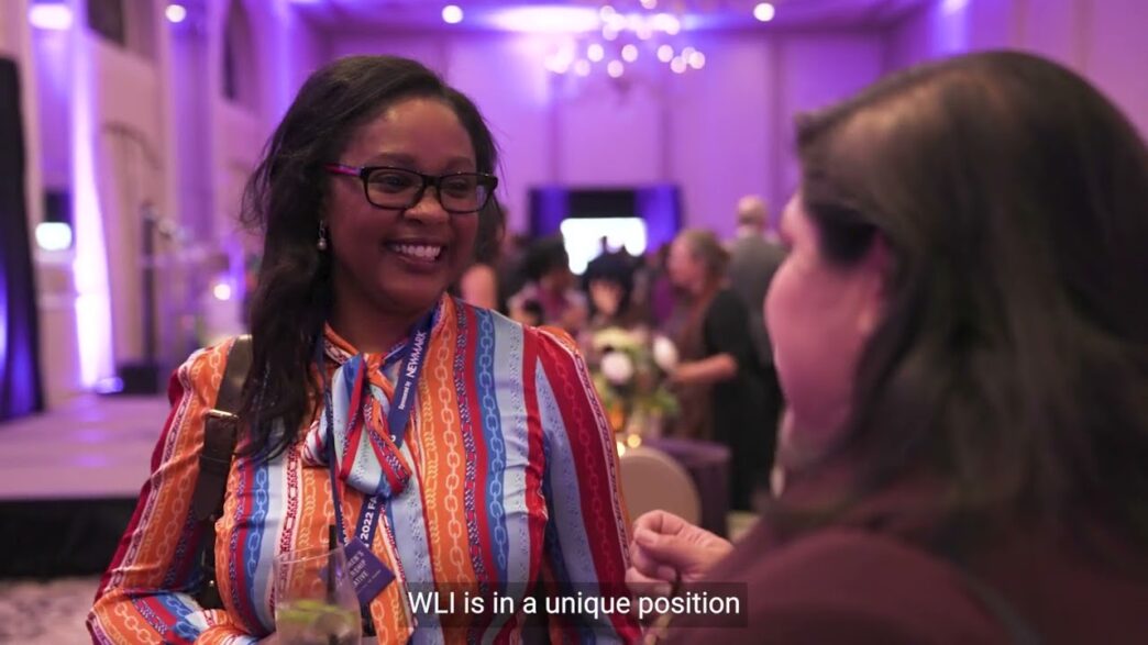 Mujer sonríe en evento de Liderazgo Femenino Real Estate. Con gafete "Newmark". Promueve el cambio necesario y visibilidad de mujeres líderes.