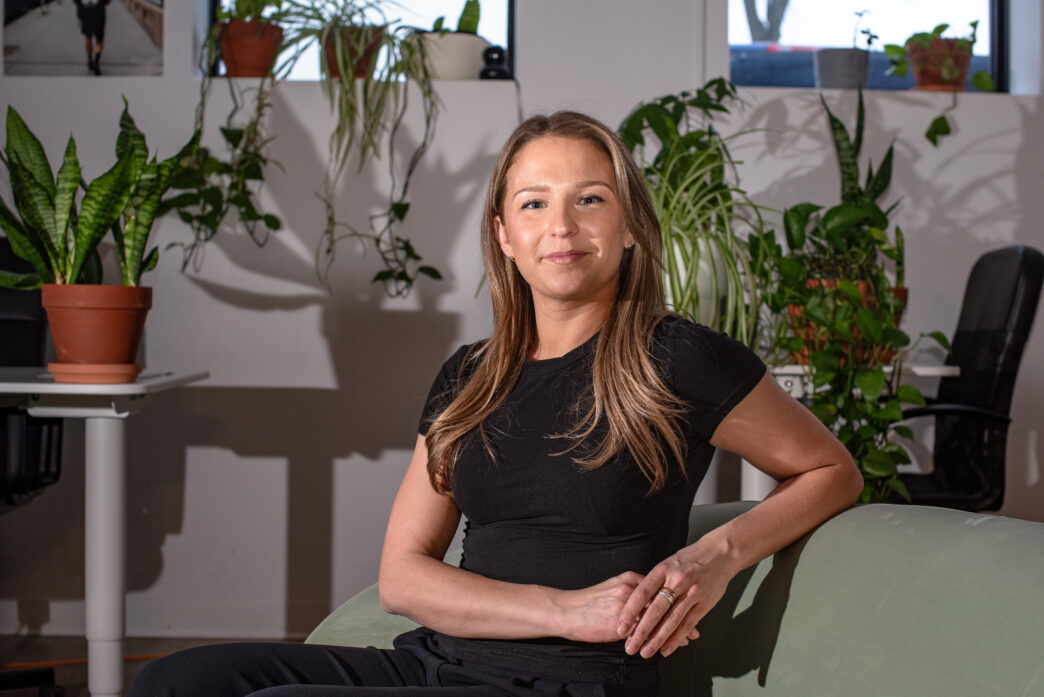Retrato de una líder femenina en el sector inmobiliario canadiense, sentada en un sillón con plantas alrededor. Transformación y éxito en bienes raíces.