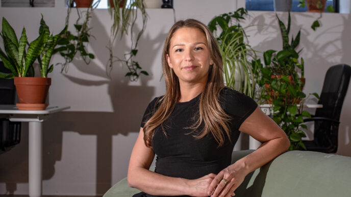 Retrato de una líder femenina en el sector inmobiliario canadiense, sentada en un sillón con plantas alrededor. Transformación y éxito en bienes raíces.