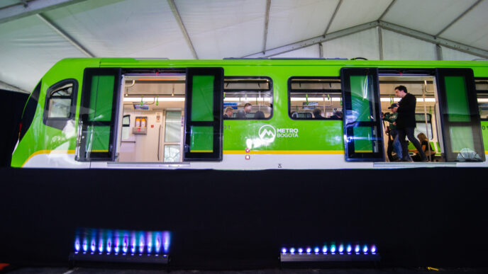 Imagen de un vagón del Metro de Bogotá, parte de la Línea 1. Se aprecia el diseño exterior en verde y blanco, con personas en el interior. Concreto.