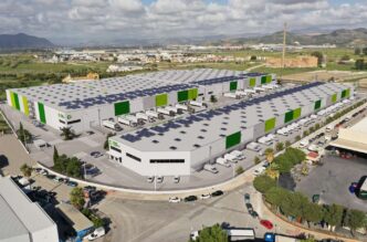 Vista aérea del parque logístico Málaga Green Logistics, con naves modernas, paneles solares y camiones. Diseño sostenible en el nuevo centro logístico.