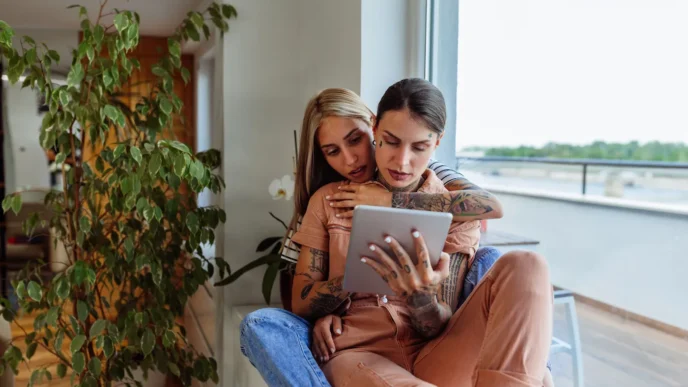 Dos mujeres revisando crédito hipotecario en tablet. Pareja del mismo sexo explora opciones de financiamiento para vivienda. Inclusión y diversidad.