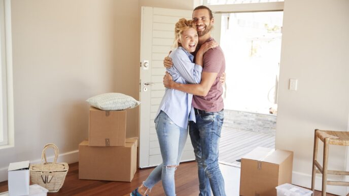 Joven pareja abrazada en su nueva casa. Millennials adquiriendo propiedades con créditos hipotecarios, celebrando su inversión inmobiliaria.