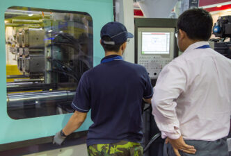 Inspección de máquina de moldeo por inyección para energías renovables. Dos técnicos observan el panel de control y el proceso de moldeo industrial.