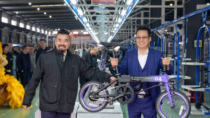 speakers/headshot
Dos hombres sonriendo sostienen una bicicleta plegable en una fábrica. Los trabajadores están de pie en segundo plano.